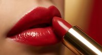 Red glossy lipstick application on female lips with golden tube, close-up beauty shot for cosmetics and makeup advertising campaigns.