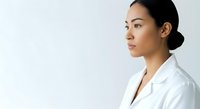 Young Asian woman wearing white lab coat in profile view against neutral background, suitable for healthcare, medical, and professional business concepts.