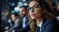 Young professional woman in glasses analyzing financial data on digital screen, business environment with bokeh lights and colleagues in background.