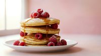 Stack of golden fluffy pancakes topped with fresh raspberries and maple syrup on white plate, breakfast food concept for restaurant menu design.