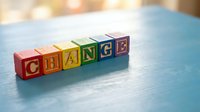 Colorful wooden alphabet blocks spelling CHANGE on blue surface with warm bokeh background for business transformation and personal growth concepts.