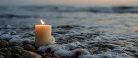 Burning candle on rocky beach at sunset with ocean waves creating peaceful meditation and remembrance atmosphere for spiritual wellness concepts.