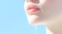 Close-up view of natural pink lips and fair skin against soft blue background, showing gentle feminine features with minimalist aesthetic composition.