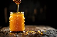 Golden honey dripping from wooden dipper into glass jar on rustic wooden surface with warm lighting for natural organic food and wellness concepts.
