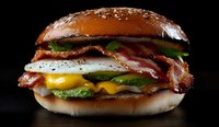 Appetizing breakfast burger with crispy bacon, melted cheese, fried egg, fresh lettuce and jalapenos on toasted sesame bun against dark background.