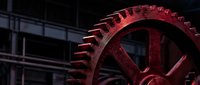 Large red industrial gear wheel in dark factory setting with metal framework background for mechanical engineering concepts.