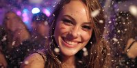 Young woman smiling at nightclub with falling confetti, colorful lights in background creating festive party atmosphere.