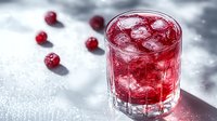 Refreshing red cocktail with ice cubes and fresh raspberries scattered on light surface. Dramatic side lighting creates appealing shadows and highlights.