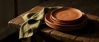 Stacked terracotta bowls with olive green linen napkin on rustic wooden table, warm natural lighting for home decor and tableware styling.