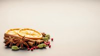 Aromatic winter spices with dried orange slices, cinnamon sticks, star anise and red berries arranged on neutral background for seasonal cooking and baking.