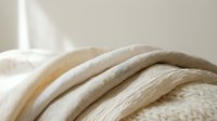 Folded natural linen and cotton fabrics in neutral beige and cream tones, showcasing soft textures and organic weave patterns for textile, interior design, and home decor projects.