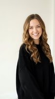 Happy young Caucasian woman with wavy blonde hair wearing black knit sweater smiling at camera against neutral beige background for lifestyle content.