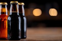 Cold beer bottles with water drops on dark wooden table against blurred lights background, moody atmosphere for restaurant or bar menu design.