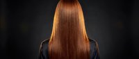 Woman with long straight glossy auburn hair viewed from behind on dark background, showcasing healthy shiny locks after salon treatment.