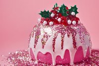 Pink Christmas ornament decorated with white dripping glaze, holly leaves, and red berries on glittery pink background, festive holiday decor element.