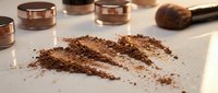 Loose bronze eyeshadow powder swatches with applicator brush and open cosmetic containers on white surface for makeup artistry and beauty product photography.