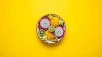Colorful tropical fruit bowl with dragon fruit, kiwi, mango, passion fruit and starfruit on vibrant yellow background, top view.
