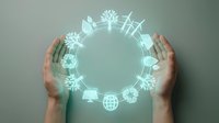 Hands protecting glowing circular hologram with environmental sustainability icons including renewable energy, recycling and green technology symbols.