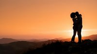 Silhouette of couple kissing on hilltop at sunset with mountains in background, romantic landscape for travel and love themed projects.