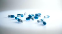 Blue and white pharmaceutical capsules scattered on white surface, suitable for healthcare, medicine, and pharmaceutical industry marketing materials.
