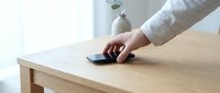 Person with hand on wireless computer mouse at wooden desk workspace with minimalist decor and natural lighting for office productivity concepts.