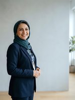 Middle Eastern woman, professional appearance, wearing dark navy blazer and headscarf, standing confidently in modern office environment with white walls and wooden flooring, suitable for corporate, business, and diversity themes.