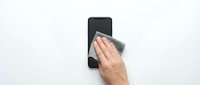 Caucasian male hand cleaning smartphone screen with microfiber cloth on white background, device maintenance and care concept.