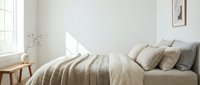 Cozy bedroom interior with striped beige bedding, decorative pillows, wooden nightstand, and natural sunlight from window. Minimalist Scandinavian design for home decor and lifestyle content.