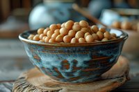Fresh chickpeas in rustic blue ceramic bowl on wooden board, shallow depth of field creates soft background blur, natural light enhances texture and color.