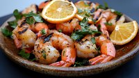 Grilled jumbo shrimp and scallops garnished with fresh parsley and lemon slices served on rustic ceramic plate, close up view of seafood appetizer.