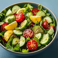 Fresh garden salad with sliced cucumbers, cherry tomatoes, yellow lemon wedges and sesame seeds served in ceramic bowl on dark background.
