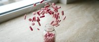 Pink capsules spilling from glass jar creating dynamic motion effect on marble surface for pharmaceutical and healthcare concepts.