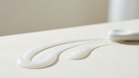 White cosmetic cream texture strokes on beige surface showing smooth skincare product consistency for beauty and wellness applications.