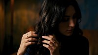 Young brunette woman with dark wavy hair touching her locks in moody dramatic lighting with warm and cool tones creating atmospheric portrait for beauty campaigns.