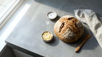 Freshly baked artisan sourdough bread loaf on wooden board with salt and butter in small bowls, ideal for bakery, food styling, and culinary content.