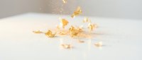 Scattered gold leaf fragments and flakes falling onto white surface, creating luxury and elegance for design, packaging, and premium branding projects.