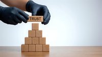 Hands in black gloves placing a wooden block labeled Trust on top of a pyramid, symbolizing leadership, reliability, and business success.