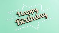 Wooden Happy Birthday lettering on mint green background with white dotted star shape, festive celebration greeting card concept.