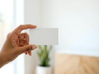 Close-up of a hand holding a blank business card in an office environment with blurred background, suitable for branding and corporate presentations.