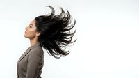 Young Asian businesswoman with flowing black hair in motion wearing gray blazer on white background for professional lifestyle concepts.