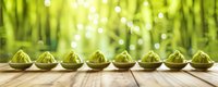 Green steamed dumplings in ceramic spoons arranged in row on wooden surface against blurred bamboo forest background with bokeh lights.