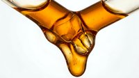 Golden amber liquid dripping and merging on white background, isolated for design use on packaging, labels, cosmetics, wellness products and advertising materials.