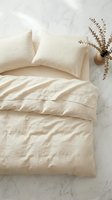 Neutral beige linen bedding set with duvet cover and pillows on marble surface with dried eucalyptus branches for minimalist bedroom interior design.