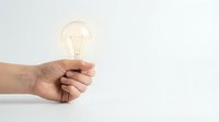 Hand holding glowing light bulb against white background symbolizing creativity innovation and bright ideas for business presentations.