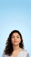 Young woman with long curly dark brown hair and olive complexion wearing lavender shirt against clear blue background for portrait and headshot use.