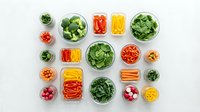Fresh vegetables and fruits organized in glass containers for healthy meal prep and food storage on white background.