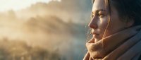Young bearded man in warm clothing gazing at golden sunset mountain landscape, contemplative mood for outdoor adventure and travel content.