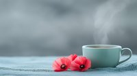 Steaming mint green cup of tea with vibrant red poppies on textured linen surface against soft blurred background creates serene morning atmosphere.