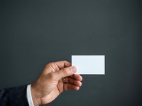 Male hand with medium skin tone holding blank white business card against dark gray background, suitable for corporate branding and professional networking materials.