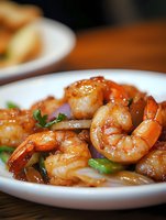 Succulent grilled shrimp in sweet and savory sauce garnished with fresh herbs on white plate, close-up view showing juicy texture and caramelized glaze.